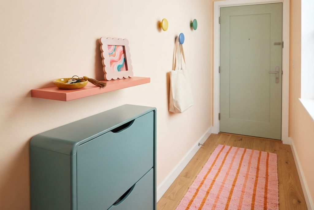 Narrow entryway with a teal shoe cabinet, coral shelf, colorful hooks, and pink-and-orange runner.